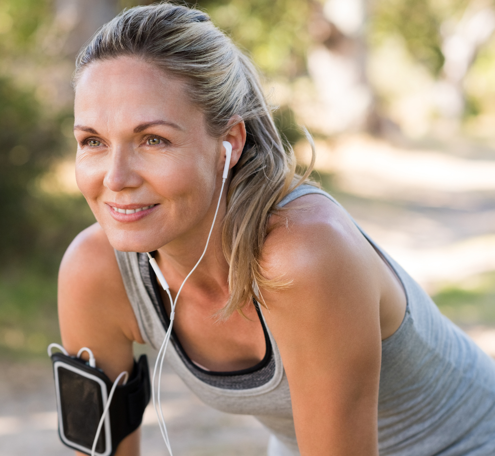 Mujer madura, atractiva, descansando después de correr, con auriculares y móvil cogido al brazo.